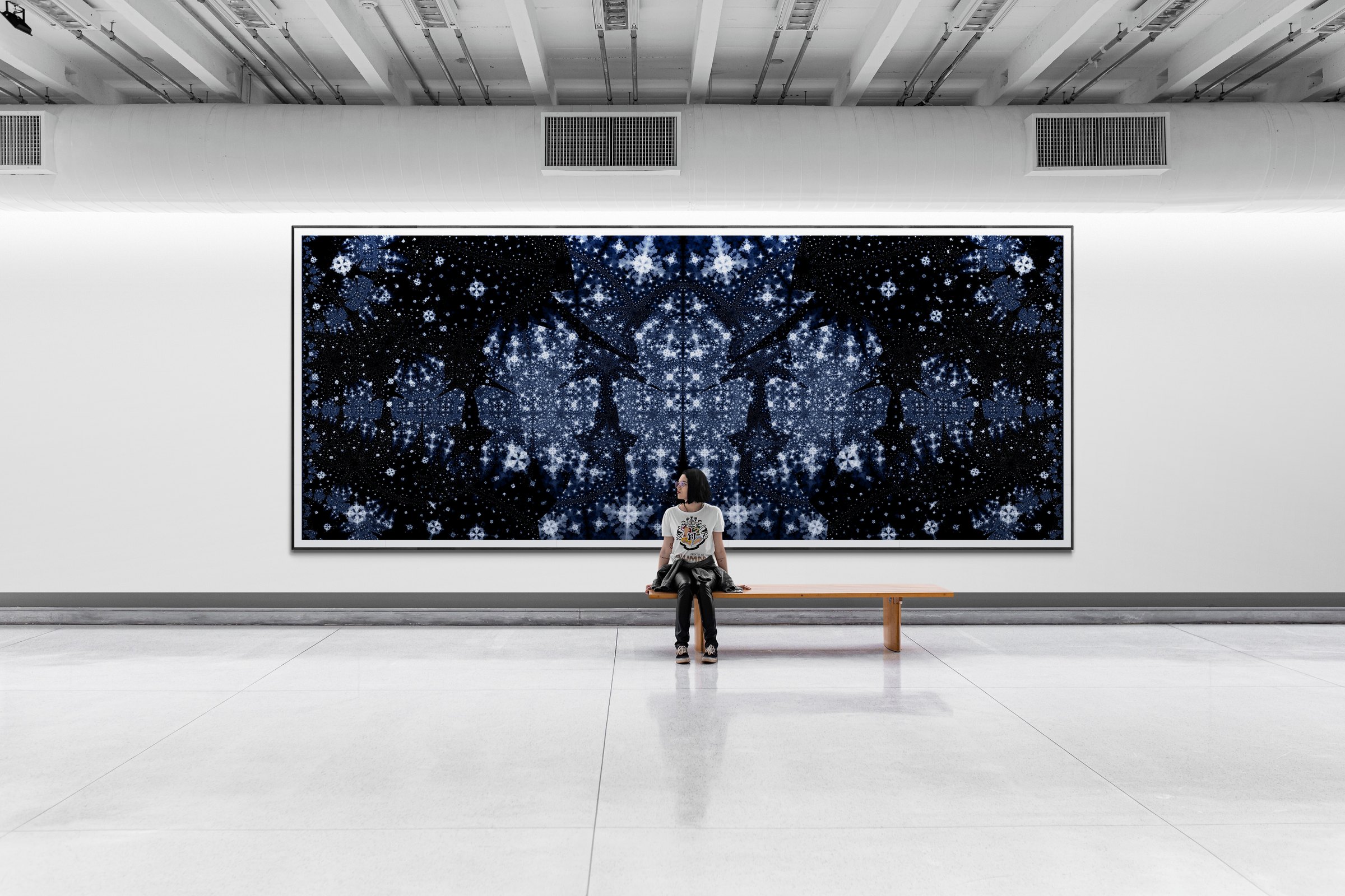 A large backlit fractal night sky installation spanning a gallery wall, a seated figure before it giving the scale.